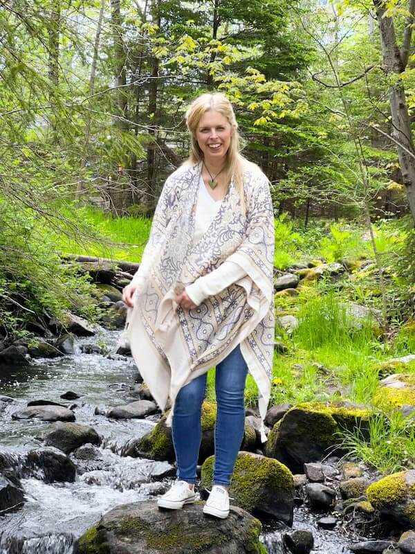 About Jill MacKay - Energy Recovery Specialist for Women, photo in nature balancing on rocks by bubbling brook in the woods smiling